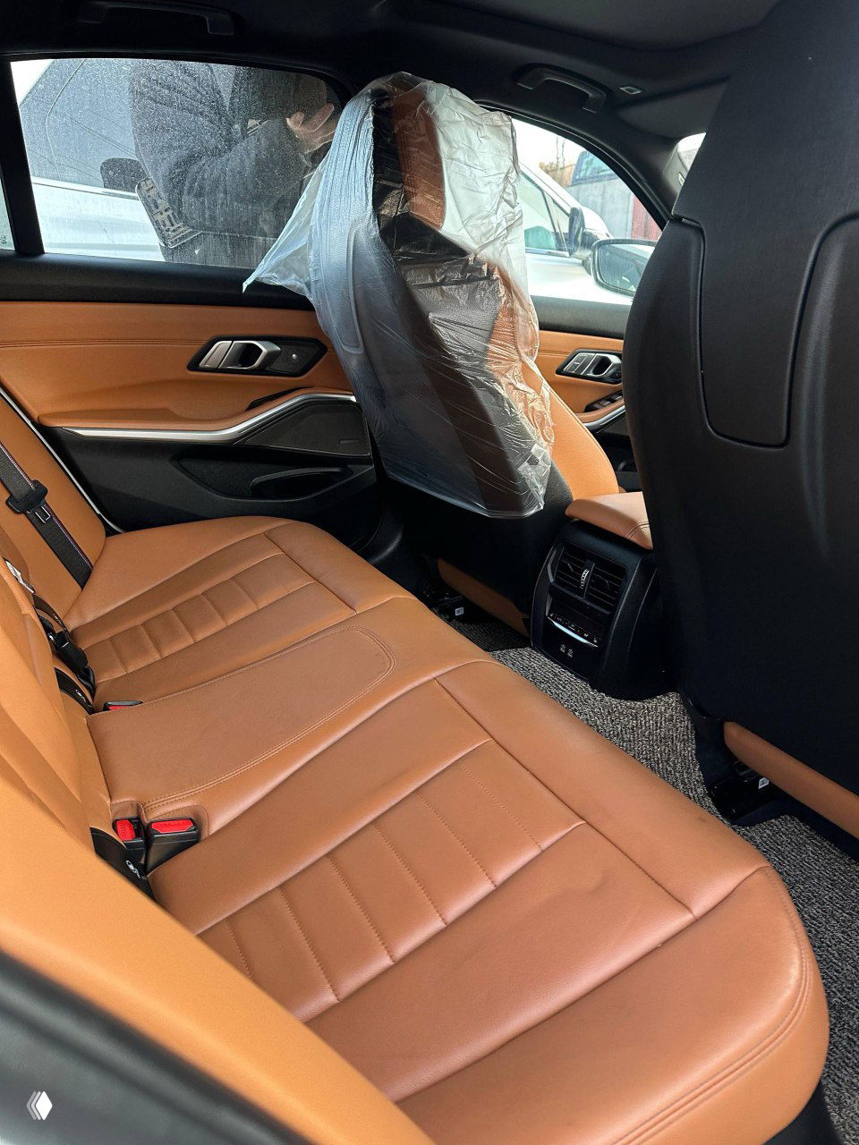 Задний ряд BMW 340i: коричневые кожаные сиденья, пространство для ног и панель задней части передних кресел — снимок сделан с открытой дверцы автомобиля перед выгрузкой.