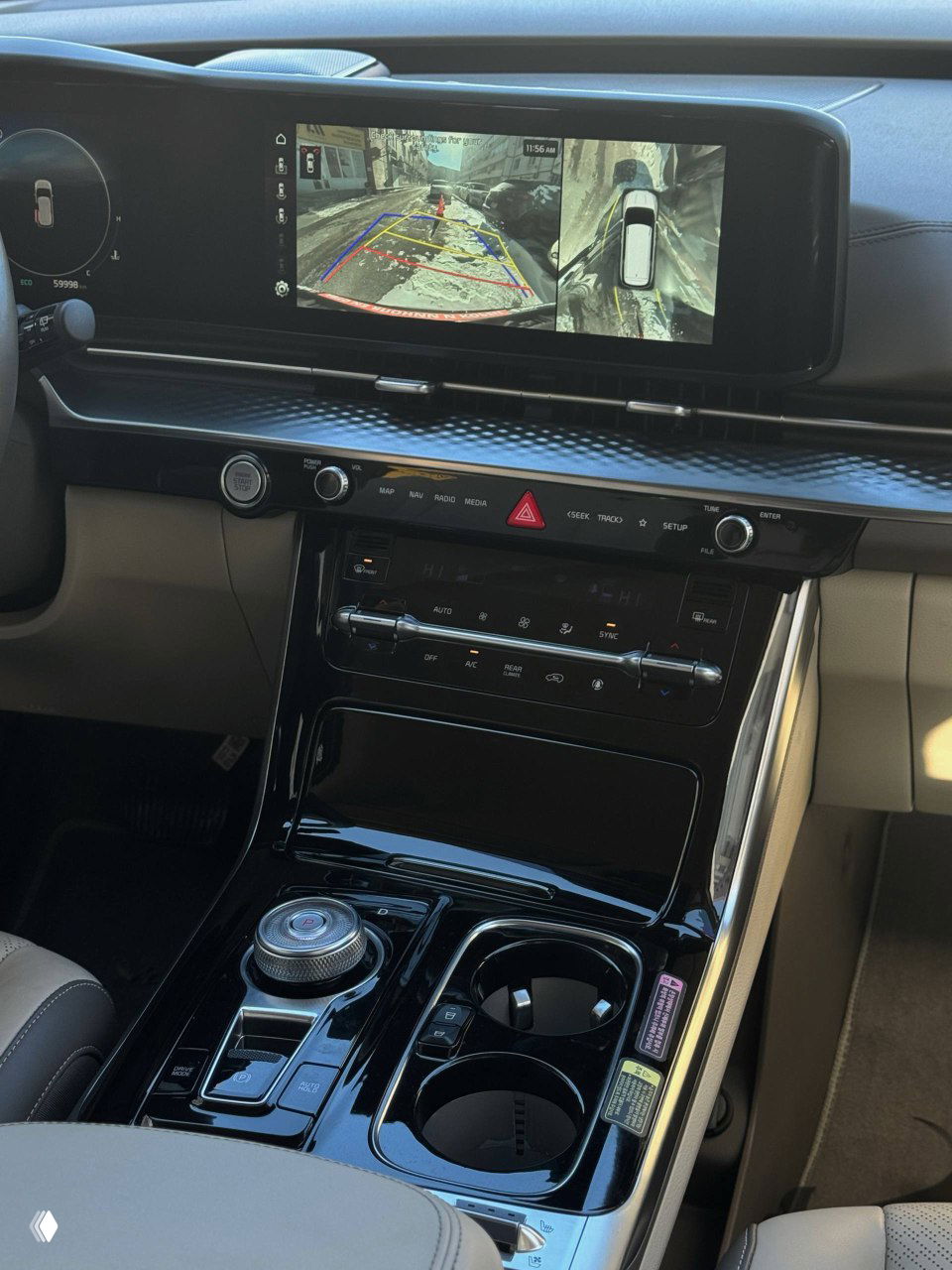 Центральная консоль KIA Carnival с большим горизонтальным экраном мультимедиа, селектором и подстаканниками крупным планом, глянцевая отделка.