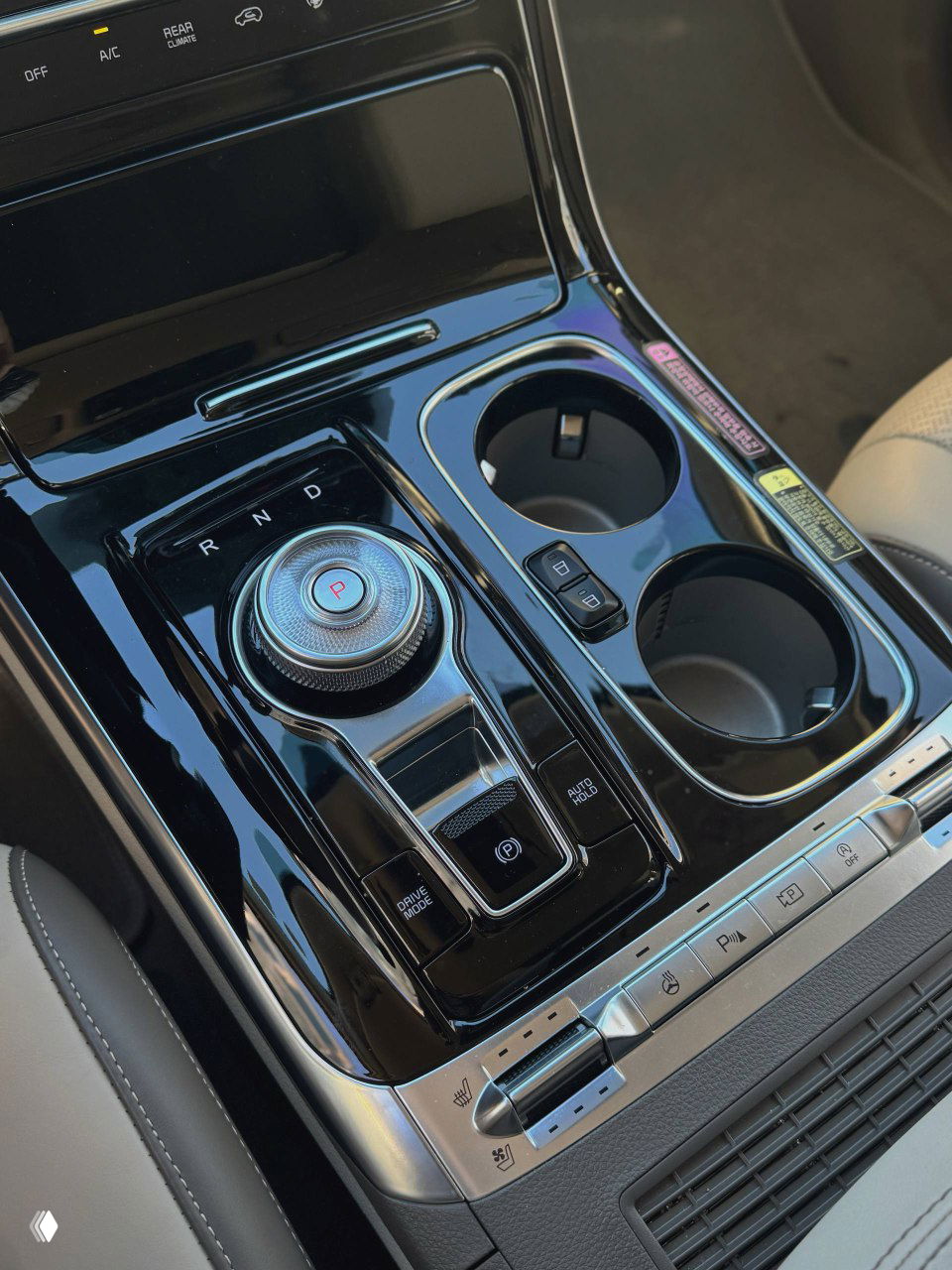 Крупный план центрального тоннеля с поворотным селектором передач, кнопками управления и двумя подстаканниками, глянцевые поверхности видны отчетливо.