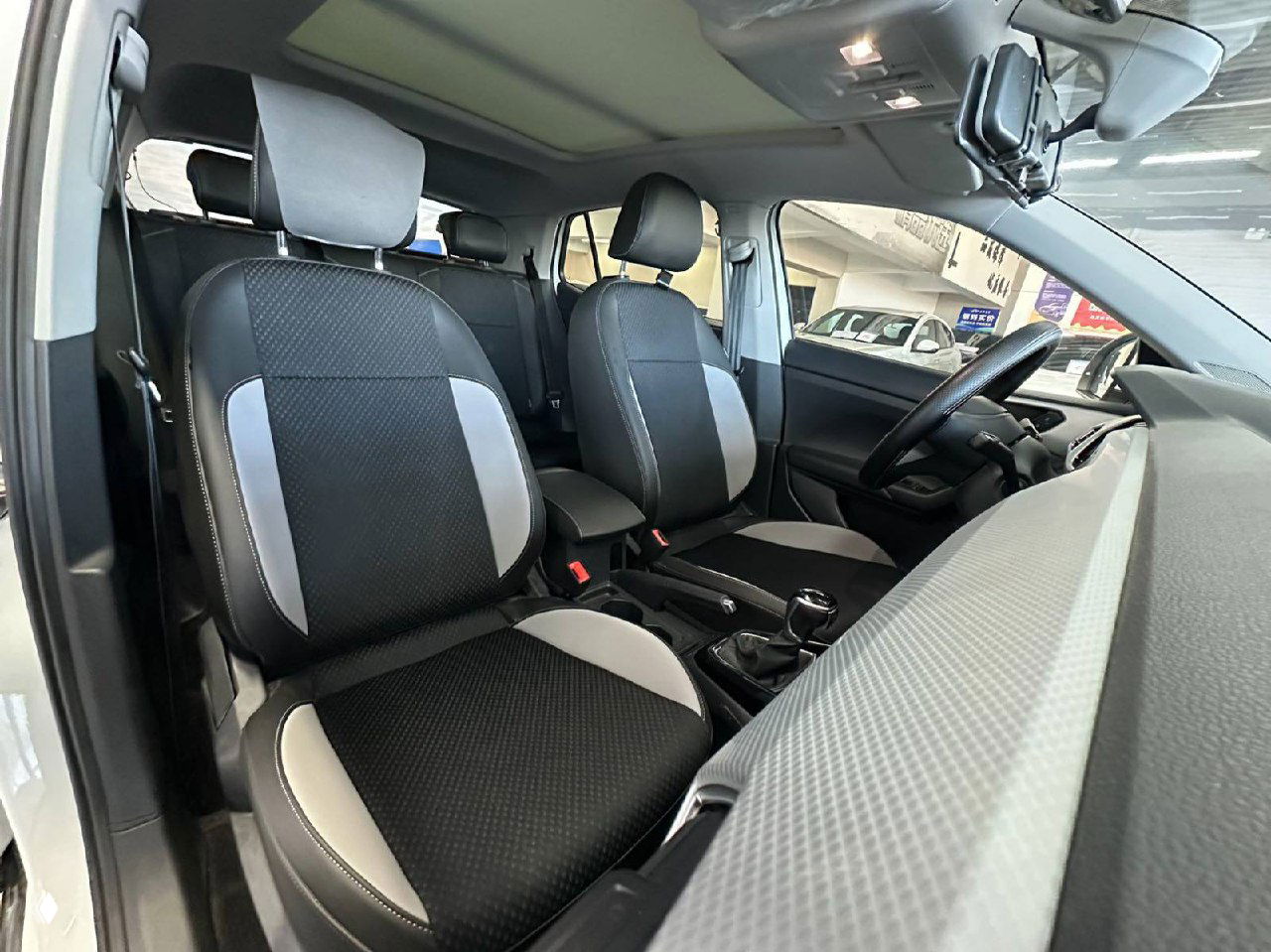 Передние сиденья и часть салона Volkswagen Tacqua: вид на обивку сидений, подлокотник и панорамную крышу в салоне автомобиля.