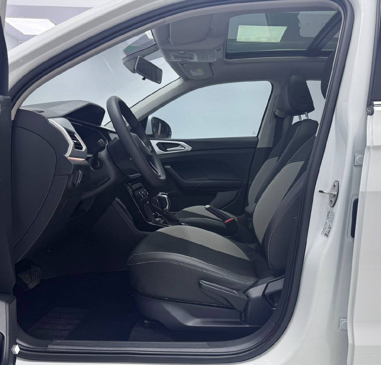 Вид через открытую переднюю дверь на салон Volkswagen Tacqua: панель приборов, рулевое колесо и переднее кресло, чистый интерьер без следов сильного износа.