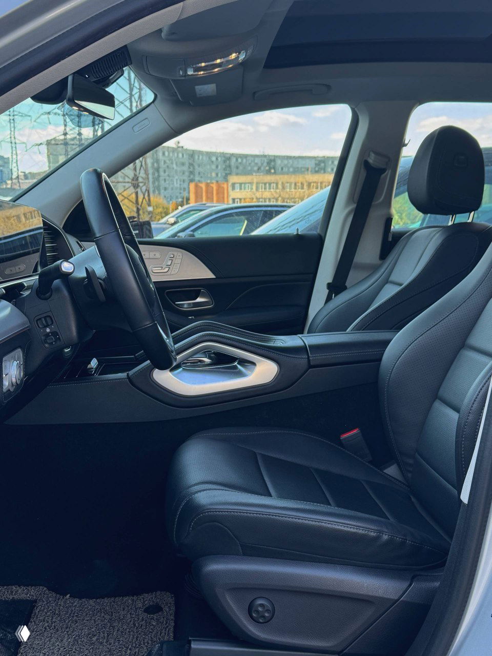 Водительское сиденье и передняя панель Mercedes GLE300d, видна отделка кожей, электрорегулировки и часть панорамной крыши на фоне парковки.