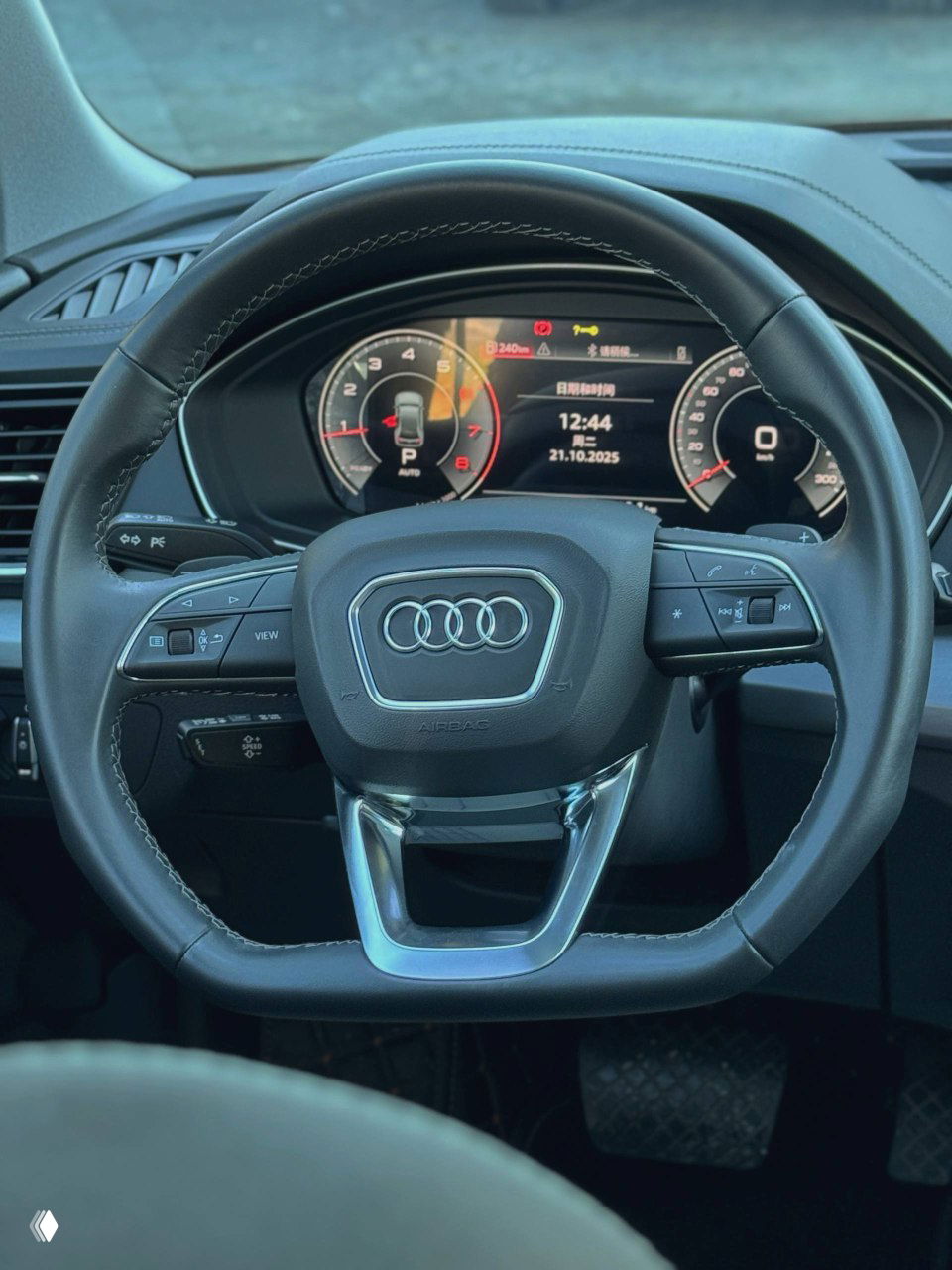 Вид на рулевое колесо Audi Q5L: кожаная отделка, кнопки управления мультимедиа и цифровая приборная панель с индикаторами и датой на экране