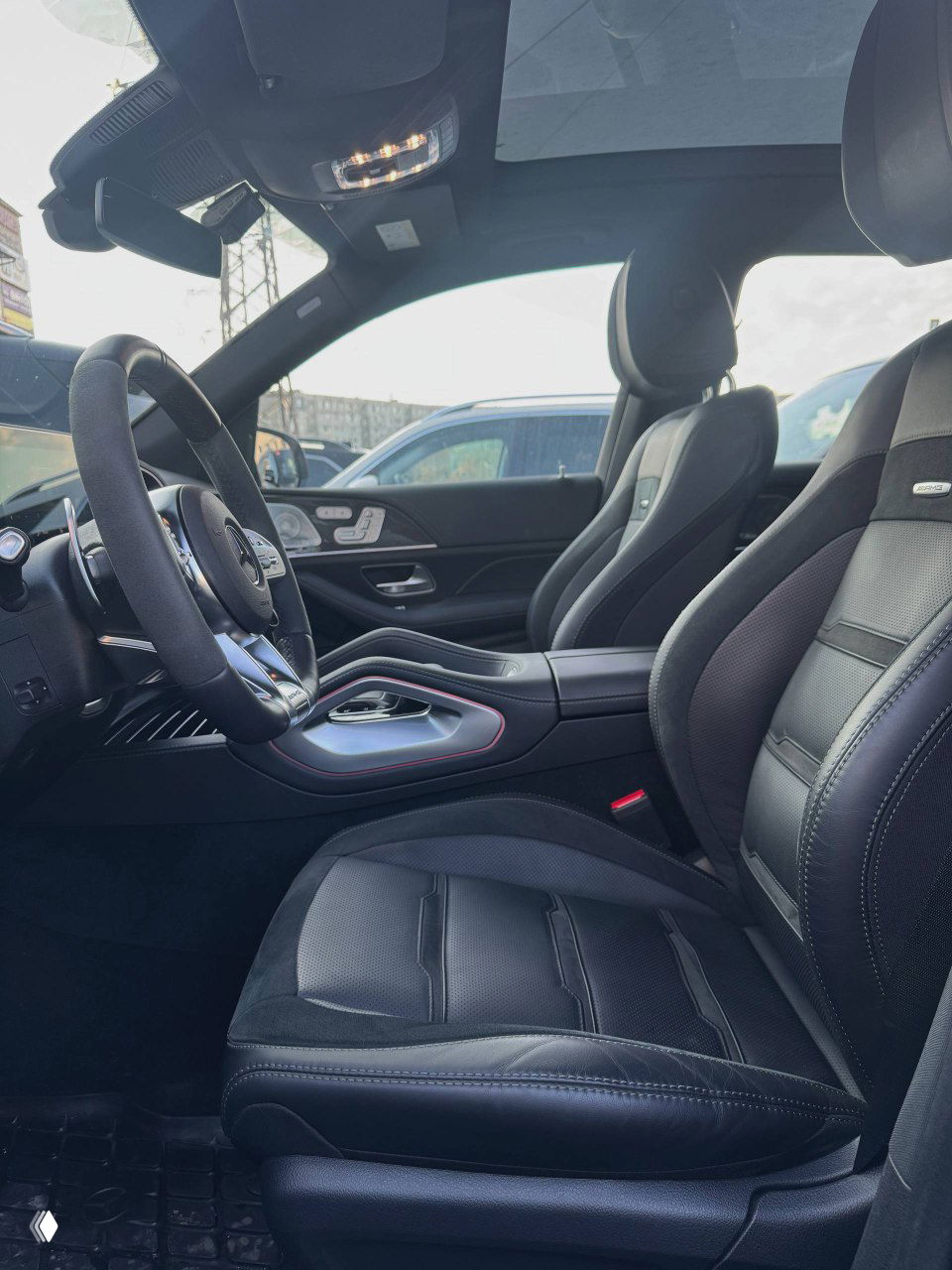 Вид на переднее пассажирское сиденье и центральный тоннель Mercedes GLE53 AMG — чёрная кожаная отделка, спортивные сиденья и панорамная крыша частично видна.