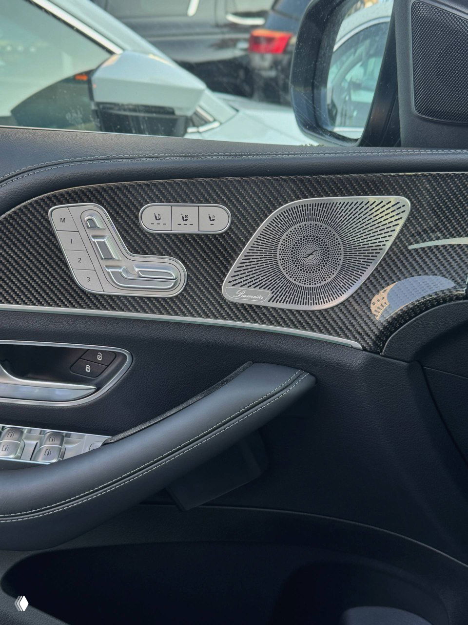 Деталь дверной карты Mercedes GLE53 AMG: декоративная вставка в карбоне, панель регулировки сиденья и динамик Burmester, чёрная отделка с прострочкой.