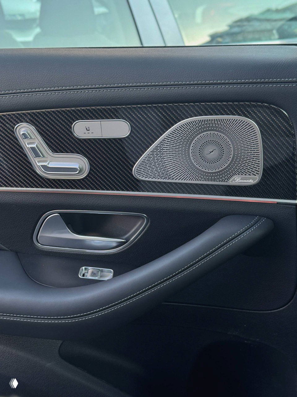 Крупный план дверной карты заднего пассажира Mercedes GLE53 AMG: карбоновые вставки, кнопки управления сиденьем и декоративный динамик с фирменной гравировкой.