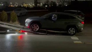 Темнота, рампа автовоза и серый Hyundai Tucson заезжает на платформу; видна дорожная разметка и отражения фар.