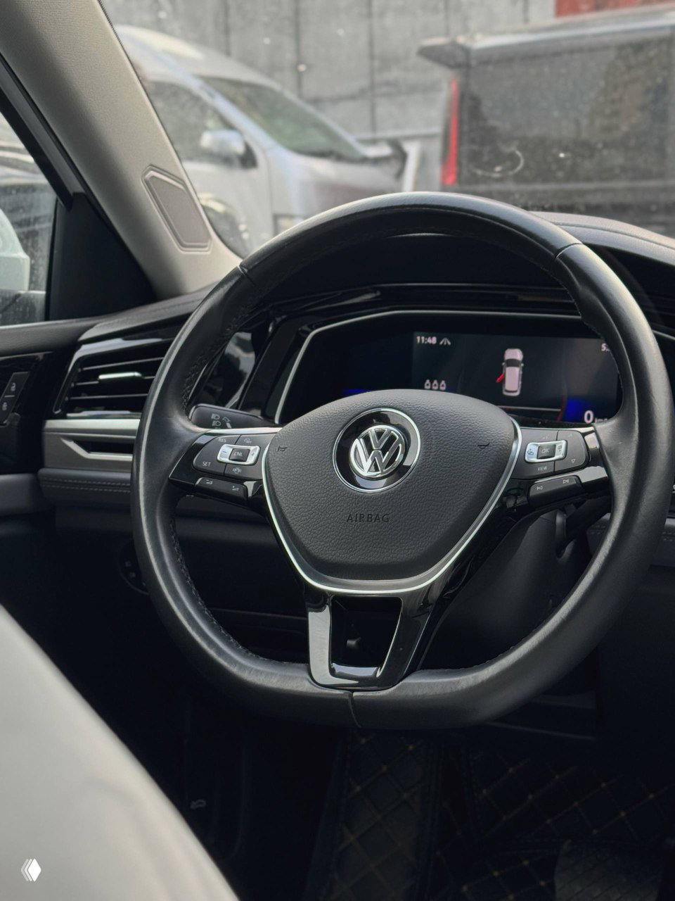 Крупный план рулевого колеса Volkswagen и части приборной панели в салоне Sagitar; видны кнопки управления и фирменная эмблема VW.