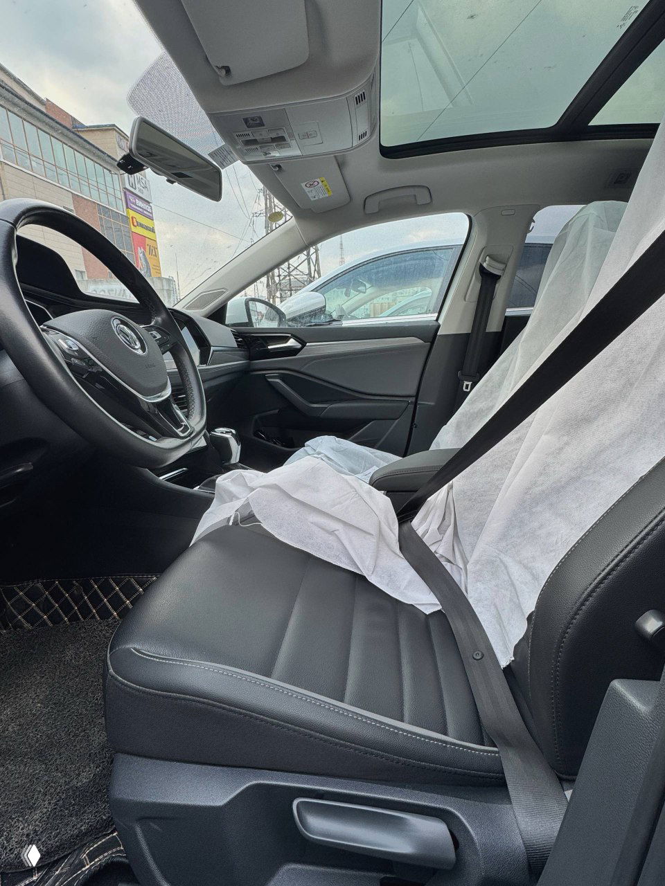 Передние сиденья и панорамная крыша Volkswagen Sagitar; видно водительское место, пассажирское сиденье и защитные чехлы на обивке.