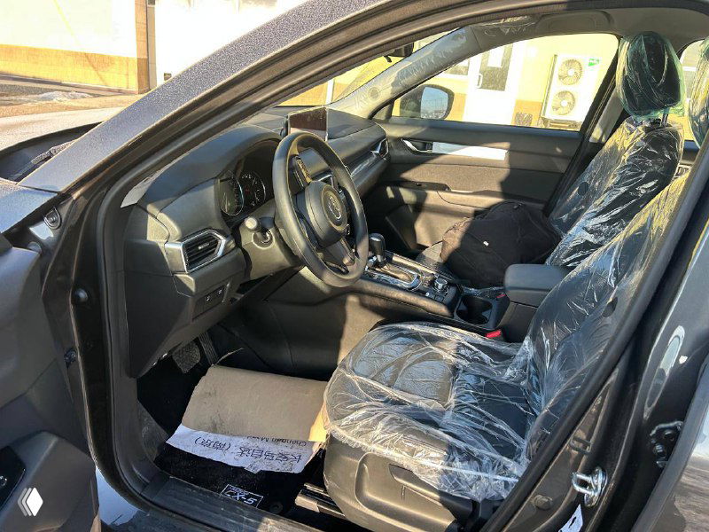 Интерьер Mazda CX-5: водительское место и передняя панель, кресла в защитной пленке после переобивки в корейскую кожу, вид через открытую дверцу.