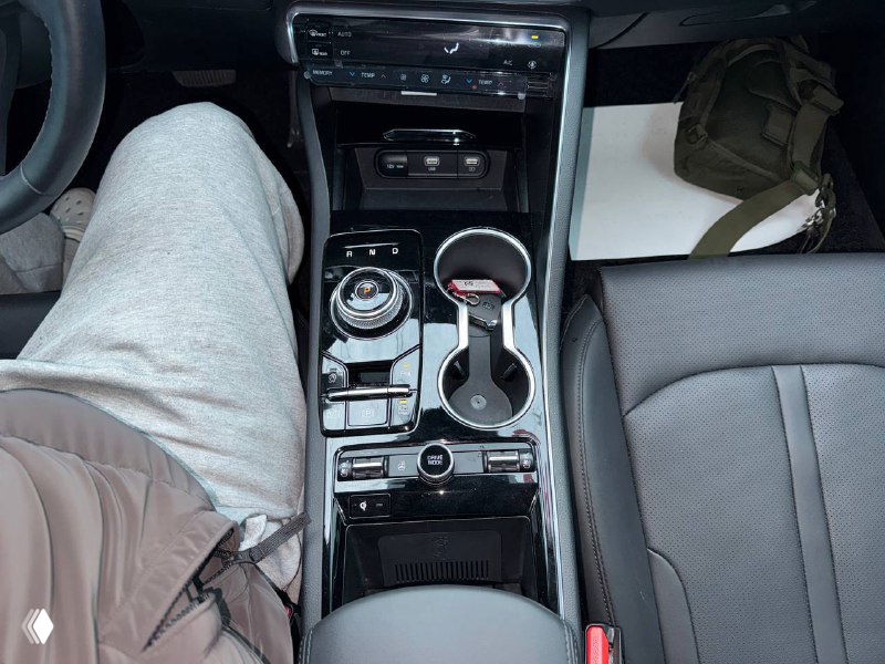 Интерьер KIA K5: центральная консоль с селектором, подстаканниками и элементами управления; вид со стороны водителя.