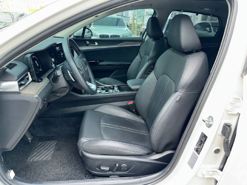 Переднее пассажирское сиденье KIA K5 в кожаной отделке, общий вид салона и панель двери на открытой стороне.