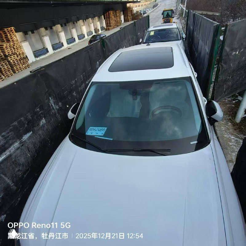 Вид сверху на белый Audi Q3 в узком проезде, видна лобовое стекло, панорамная крыша и парковочные ограждения.