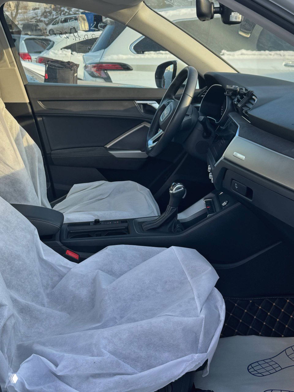 Вид салона Audi Q3 с центральным тоннелем и передними сиденьями, защитные чехлы и коврики на полу