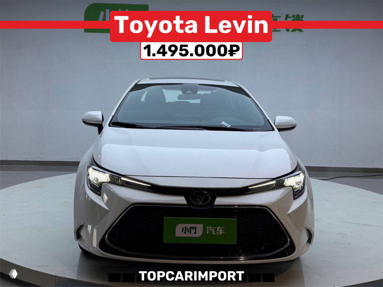 Фронтальный вид белой Toyota Levin в выставочном павильоне, хорошо видна решётка и фары, цена 1.495.000₽ указана на баннере
