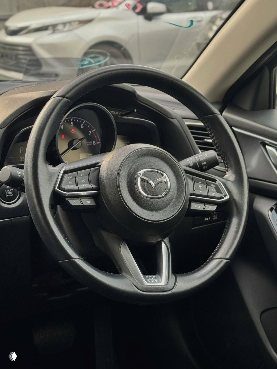 Руль и панель управления Mazda Axela — крупный план рулевого колеса с логотипом Mazda, элементы управления и часть приборной панели, состояние салона.