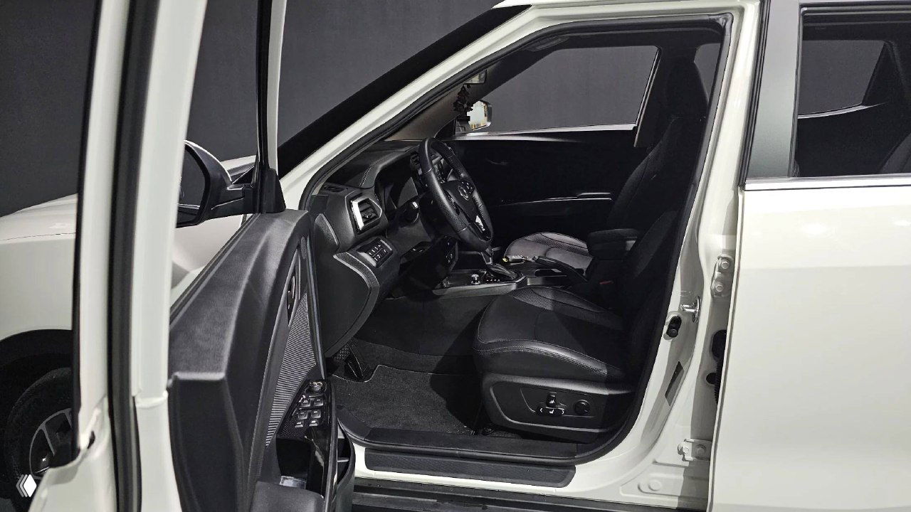 Открытая передняя дверь и вид на водительское сиденье Tivoli; видно регулировки сиденья, дверную панель и общий обзор рабочего места водителя.