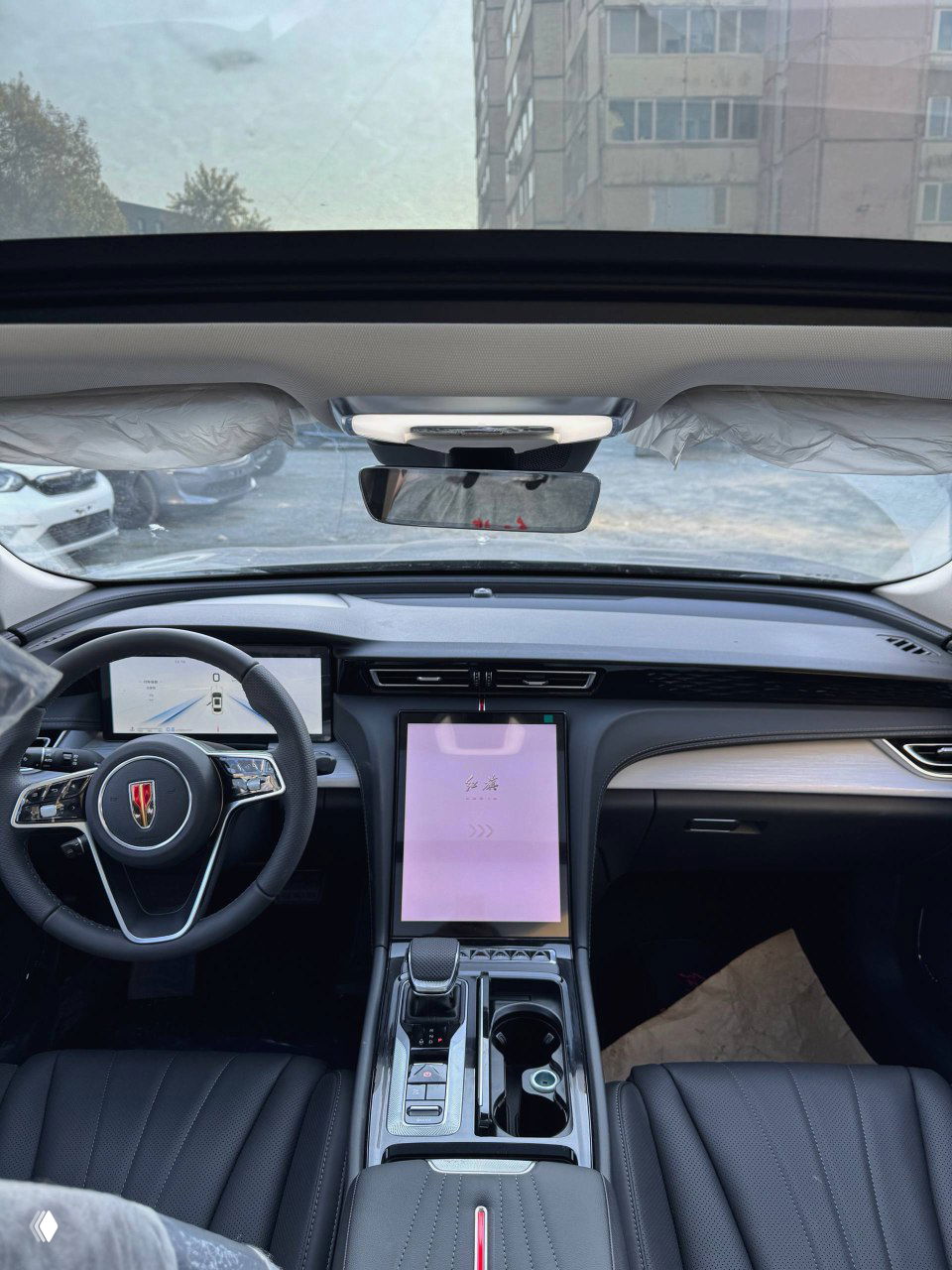 Панорамный вид торпедо и передней части салона Hongqi H5: рулевая колонка, экран водителя и потолочный зеркальный модуль.