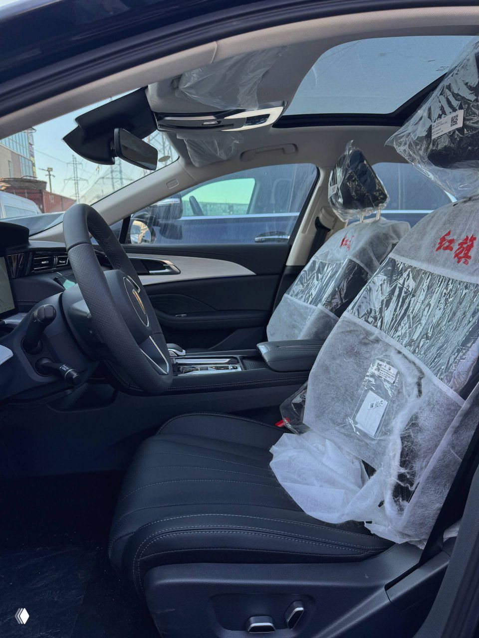 Вид на передние сиденья Hongqi H5 с защитной плёнкой, боковые панели и панорамная крыша; интерьер в заводской подготовке к доставке.