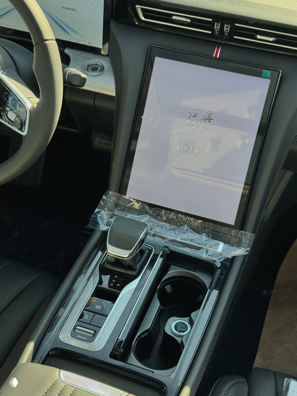 Крупный план селектора коробки передач и центрального подстаканника Hongqi H5, защитная плёнка на элементах передней консоли.