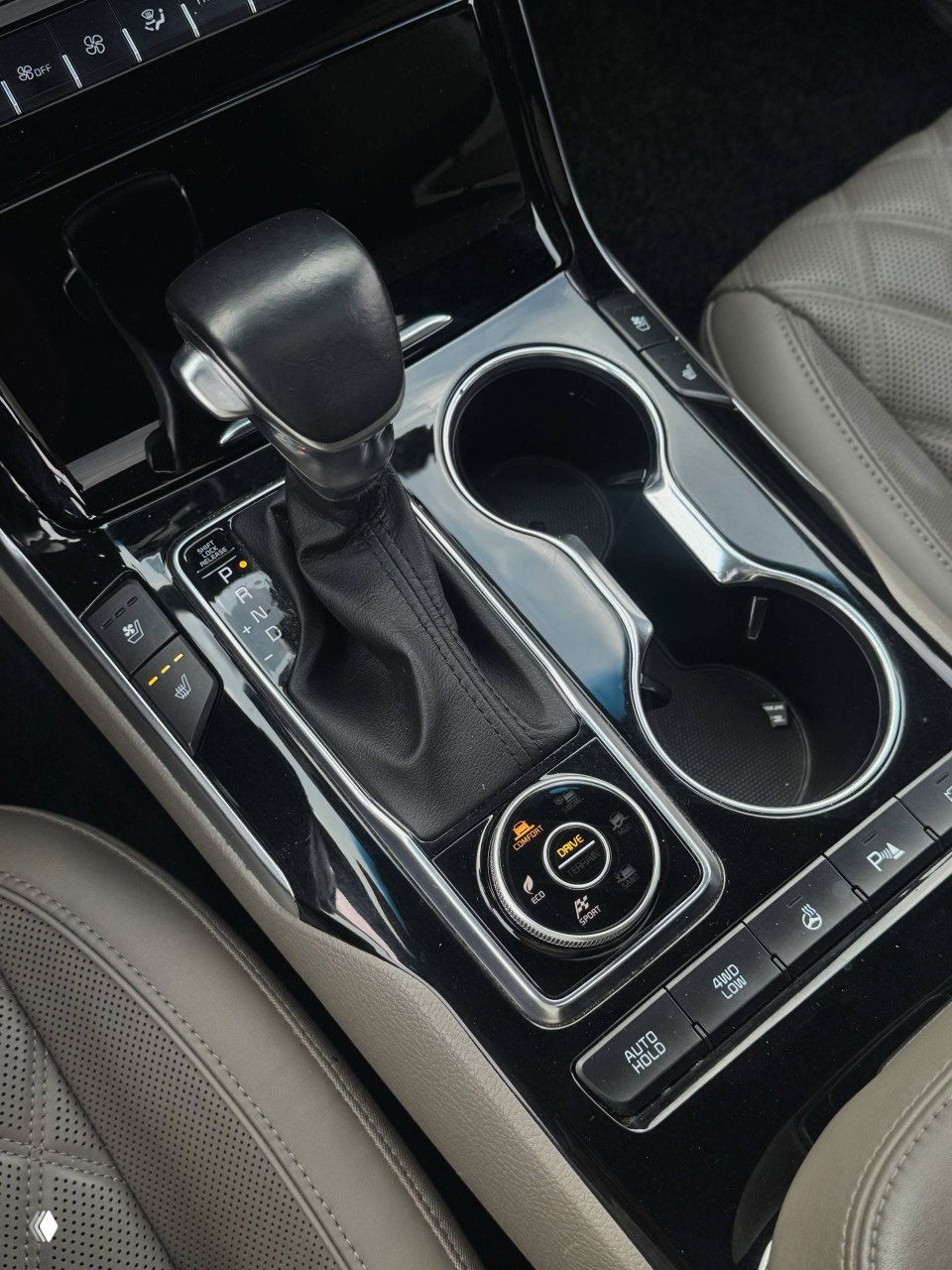 Рычаг передач и подстаканники KIA Mohave The Master, крупный план на глянцевую поверхность центрального туннеля и элементы управления.