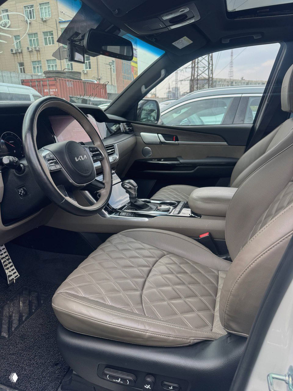 Вид на переднее левое кресло и центральный тоннель KIA Mohave, кожа сидений с ромбовидной прострочкой и элементы управления.