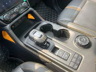 Центральная консоль Ford Ranger с селектором передач, подстаканниками, круговым регулятором режимов и кожаной отделкой, интерьер крупным планом.