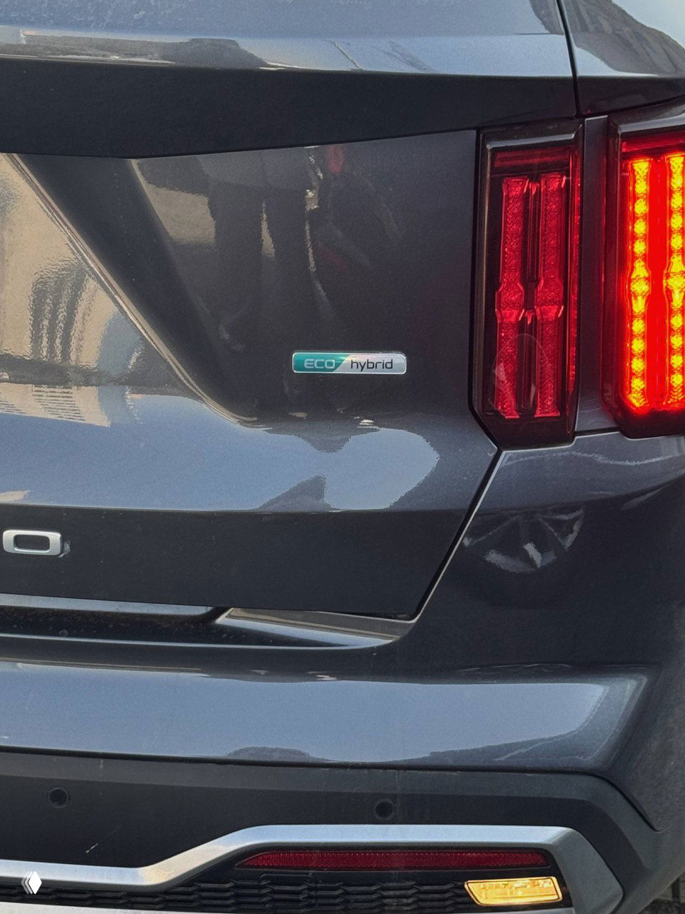 Задняя часть KIA Sorento с эмблемой ECO hybrid — крупный план заднего бампера и значка «ECO hybrid», отражение окружающей среды на лаке.