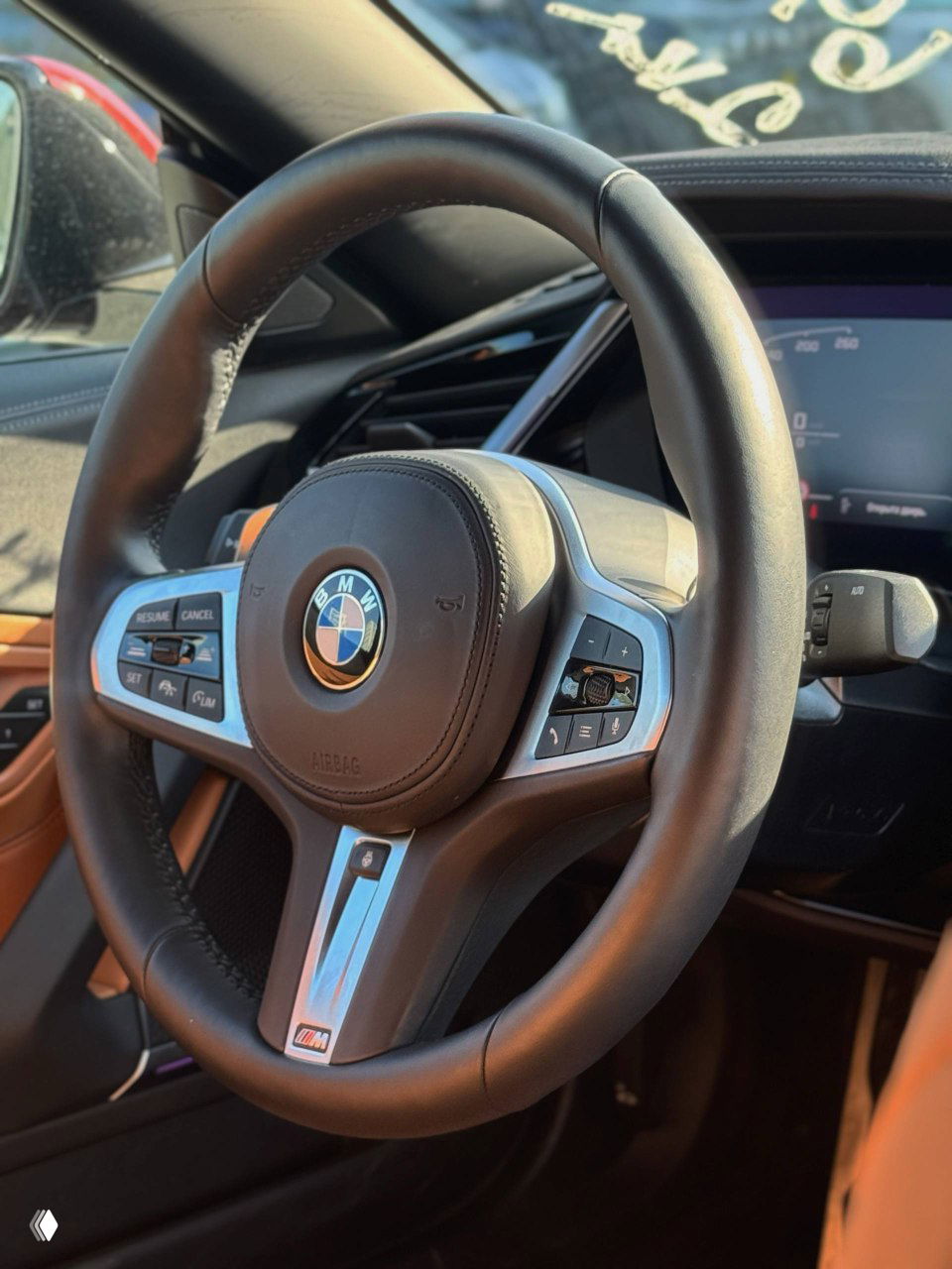Крупный план рулевого колеса BMW с эмблемой и элементами управления, чёрная кожа и хромированные вставки на мультируле M‑Sport.