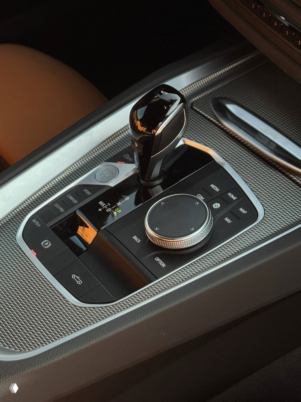 Блок управления коробкой передач и центральный консольный джойстик iDrive на фоне текстурной серебристой отделки и кнопок режима.