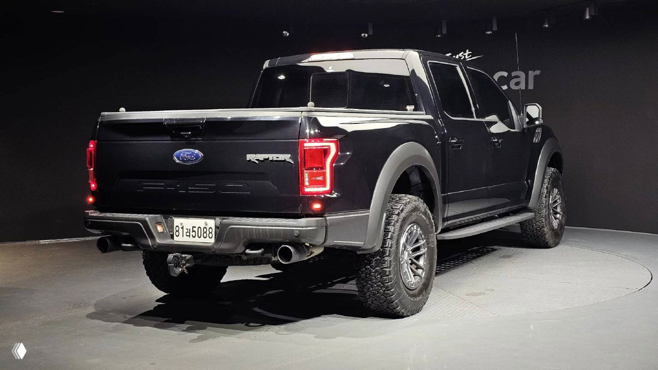 Задняя часть чёрного Ford F-150 Raptor 2020 в шоуруме, вид на платформу, выхлопные патрубки и задние фонари модели
