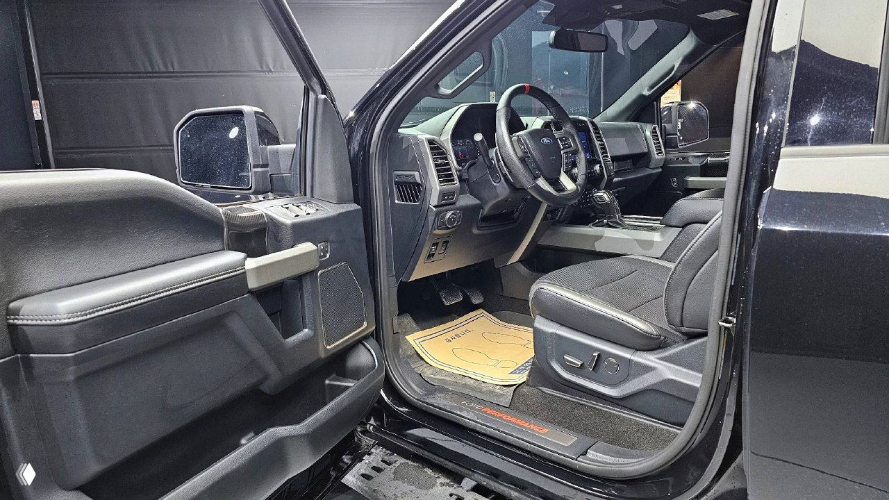 Открытая передняя дверь и вид на водительское сиденье Ford F-150 Raptor 2020: панель двери, руль и кресло со ступенчатой посадкой