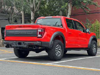 Задняя часть красного Ford F-150 Raptor на парковке; видны крупный борт, фонарь, буксировочные точки и рельефный дизайн заднего бампера.
