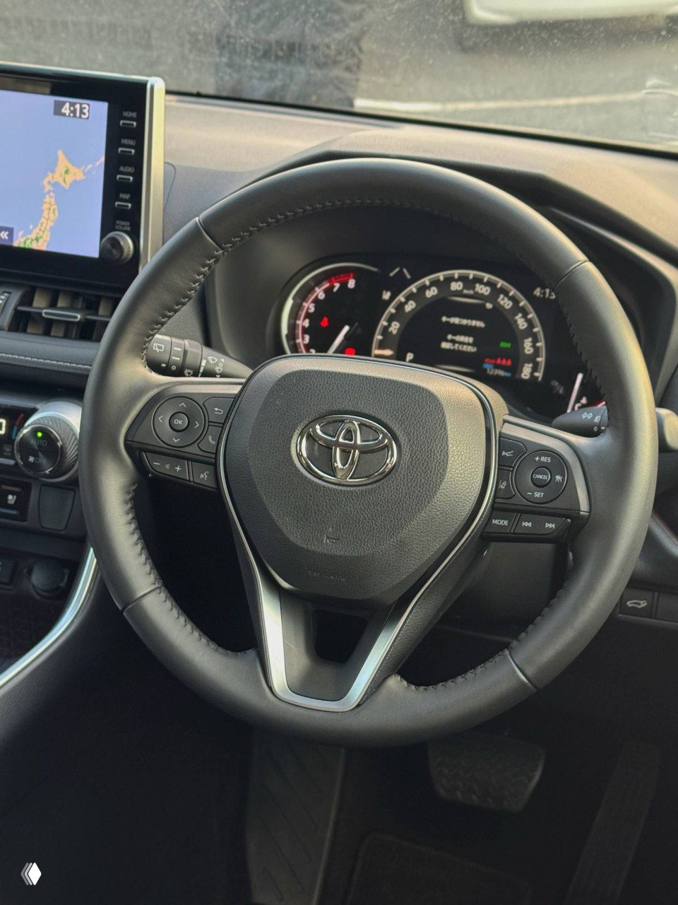 Рулевое колесо Toyota с логотипом Toyota и множеством кнопок управления (круиз-контроль, мультимедиа); вид панели приборов и части руля в салоне автомобиля.