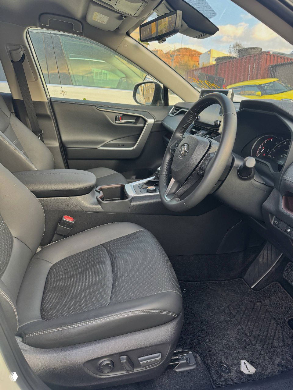 Переднее сиденье и центральный подлокотник Toyota RAV4 — обзор на пассажирское место, роялка отделки сидений, чистый салон и коврики без следов эксплуатации.