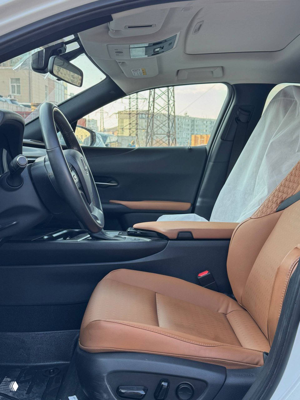 Переднее сиденье с коричневой кожаной отделкой в салоне Lexus UX200; видно панорамный вид на приборную панель и водительскую зону.