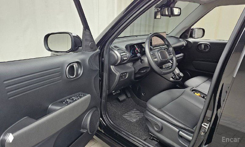 Открытая передняя дверь Hyundai Casper и вид на водительское место, рулевое колесо, кресло и внутреннюю отделку — интерьер со стороны водителя.