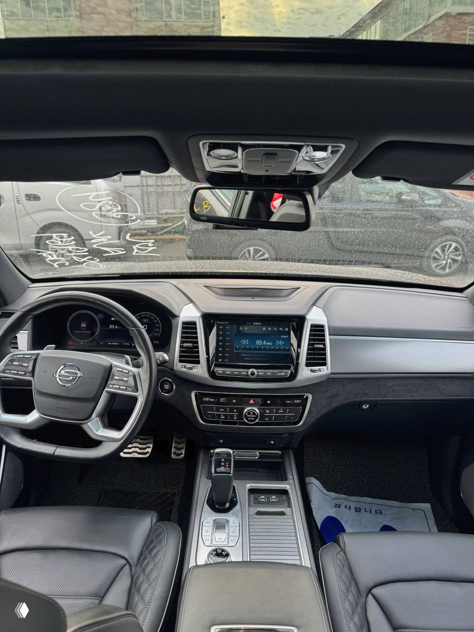 Передняя панель и центральная консоль SsangYong NEW Rexton: мультимедийный экран, дефлекторы и зеркало заднего вида, интерьер в тёмных тонах.