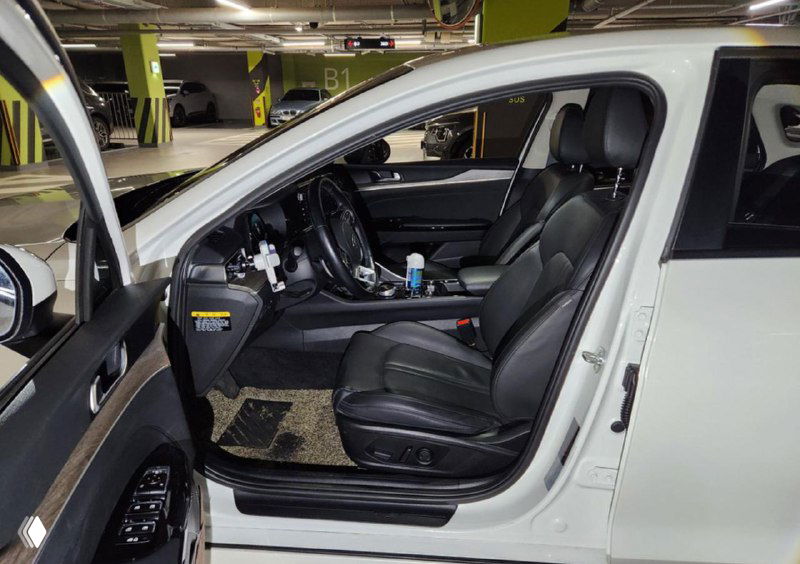 Фотография водительского места белого автомобиля: сиденье, руль, консоль и коврик — видна общая сохранность интерьера.