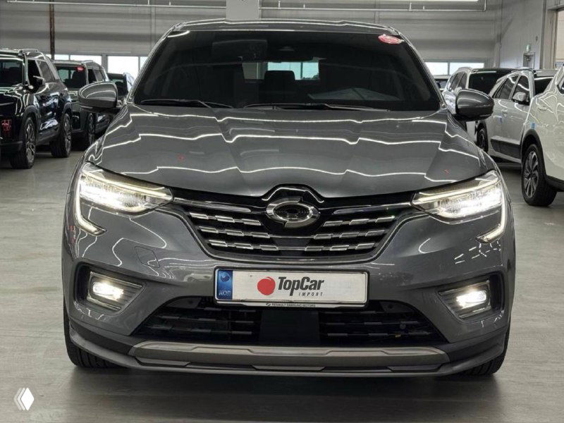 Фронтальный снимок серого автомобиля в шоуруме с листинг-рамкой TopCar; видно освещение и аккуратный внешний вид автомобиля.