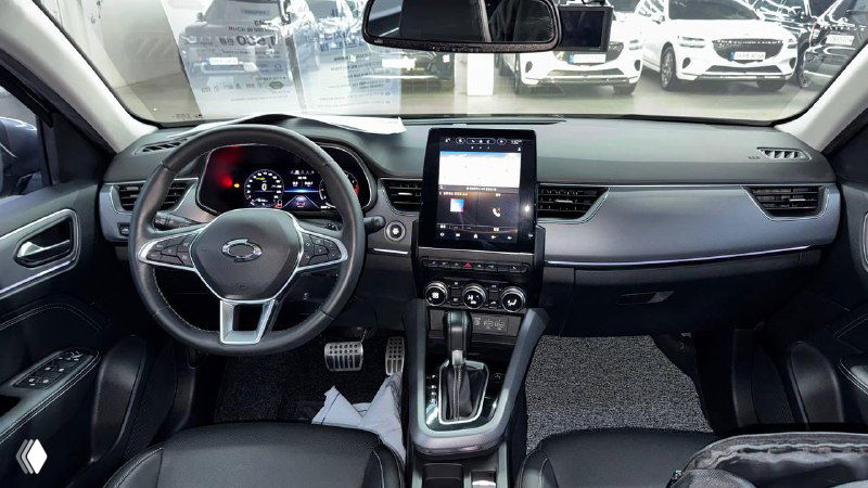 Снимок центральной консоли и приборной панели серого автомобиля в салоне дилерского центра; видно экран, переключатели и отделку.