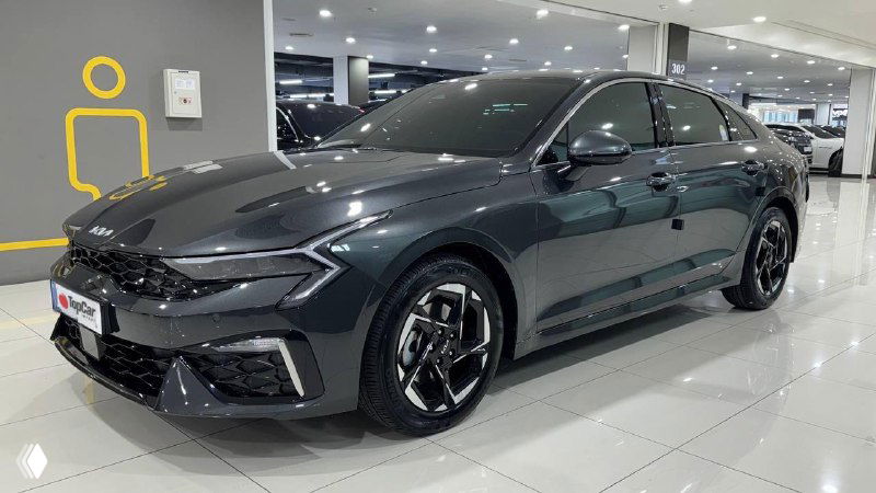 Боковой вид тёмного седана в дилерском шоуруме: видны колёса, боковые линии кузова и общий профиль автомобиля.