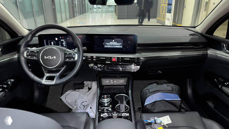 Фото интерьера тёмного седана: приборная панель, руль и центральный тоннель с видимыми предметами на сиденье и ковриках.