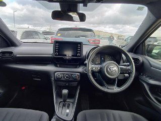 Интерьер Toyota Yaris 2021: вид на панель приборов, мультимедиа‑экран и руль; видно состояние приборной панели и передней части салона.