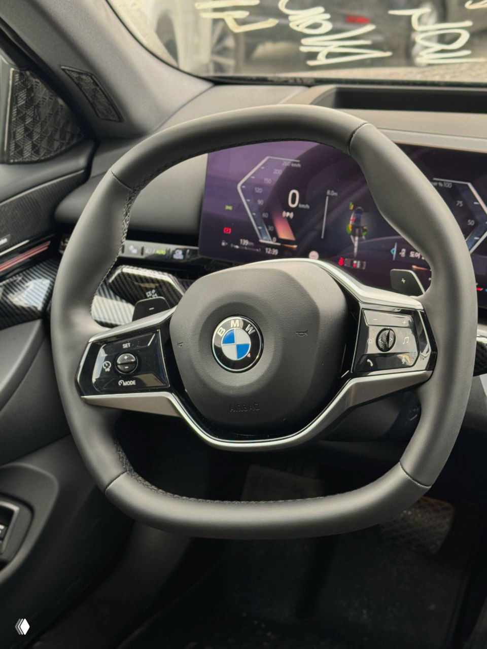 Рулевое колесо BMW с логотипом в центре, на фоне видна цифровая приборная панель и часть торпедо с элементами управления.