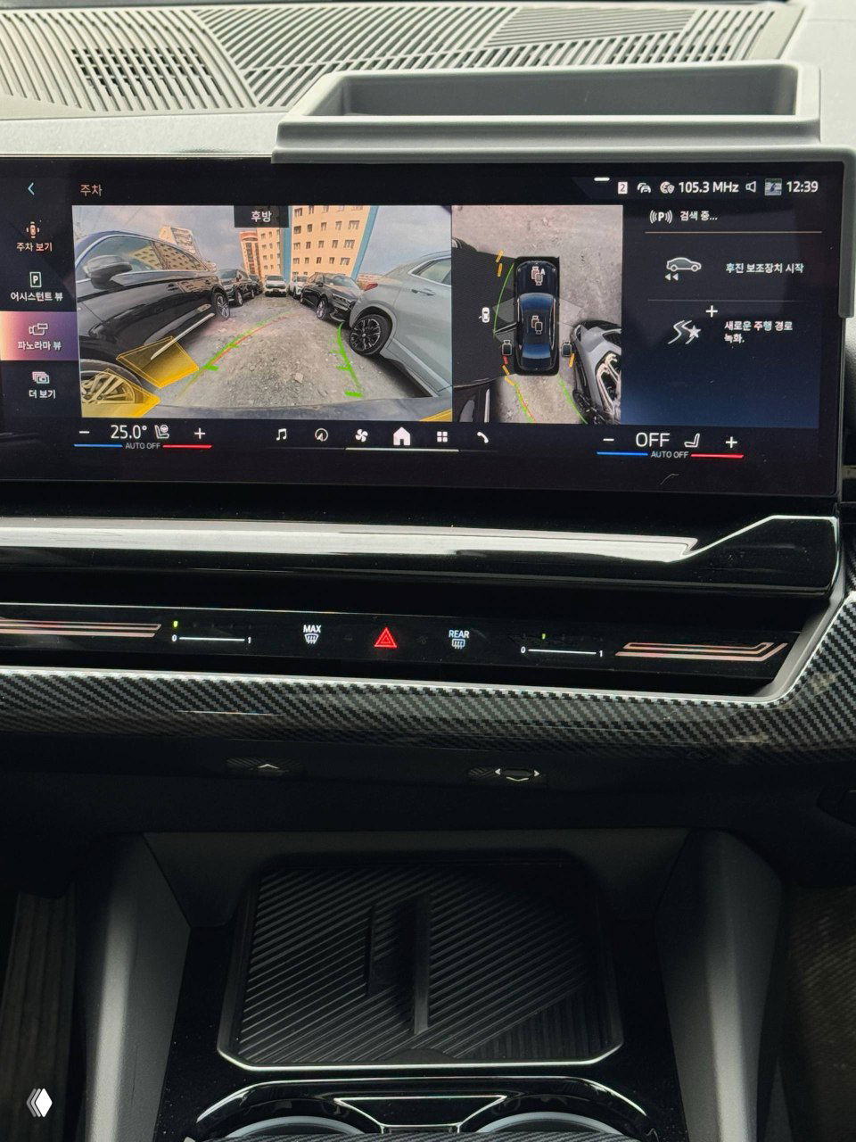 Широкоформатный экран мультимедиа BMW с изображением камеры заднего вида и панорамного обзора паркинга, видна панель климата.