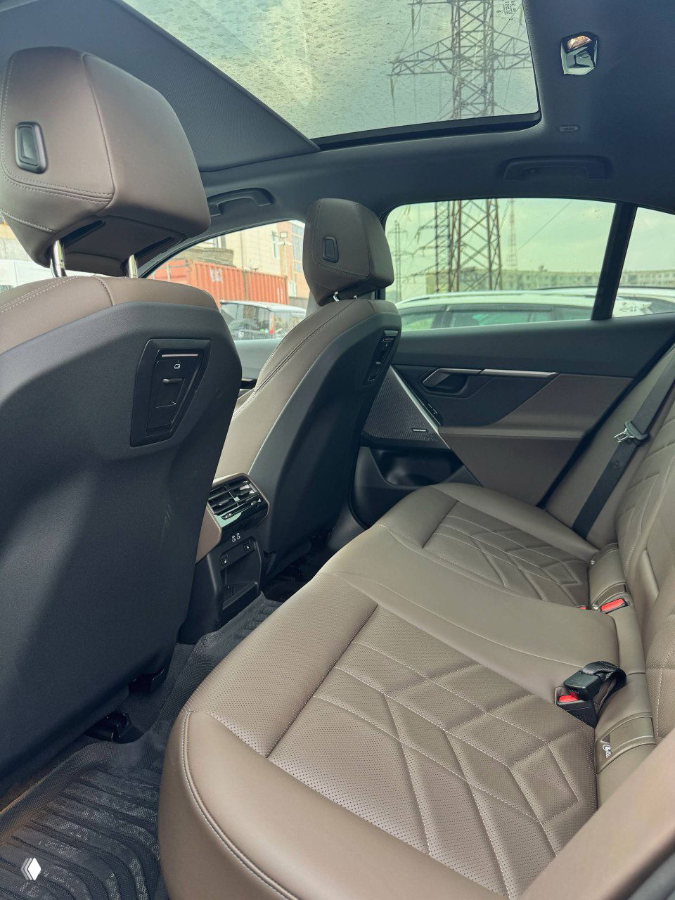 Задний ряд сидений BMW с коричневой кожаной обивкой, видно пространство для ног и панорамный люк над салоном автомобиля.