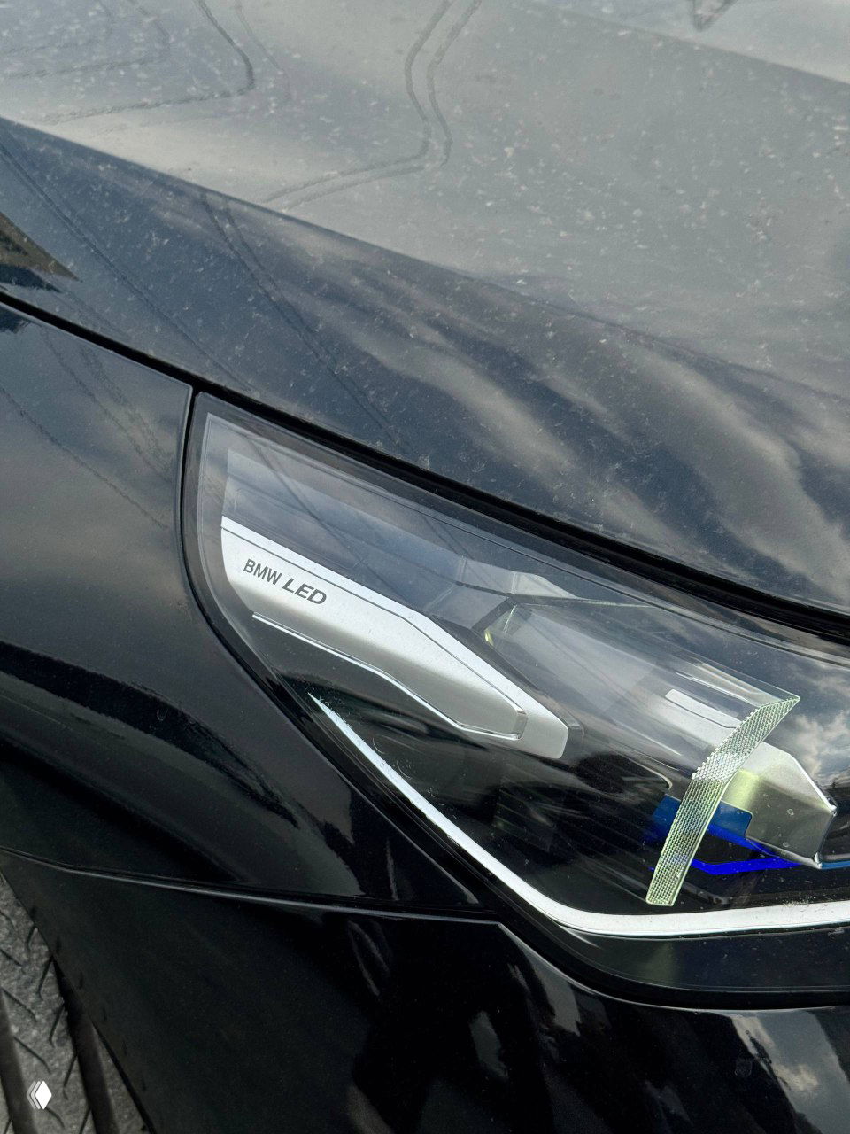 Крупный план передней LED-фары BMW с маркировкой BMW LED, видно отражение неба на лаке кузова и детали корпуса фонаря.