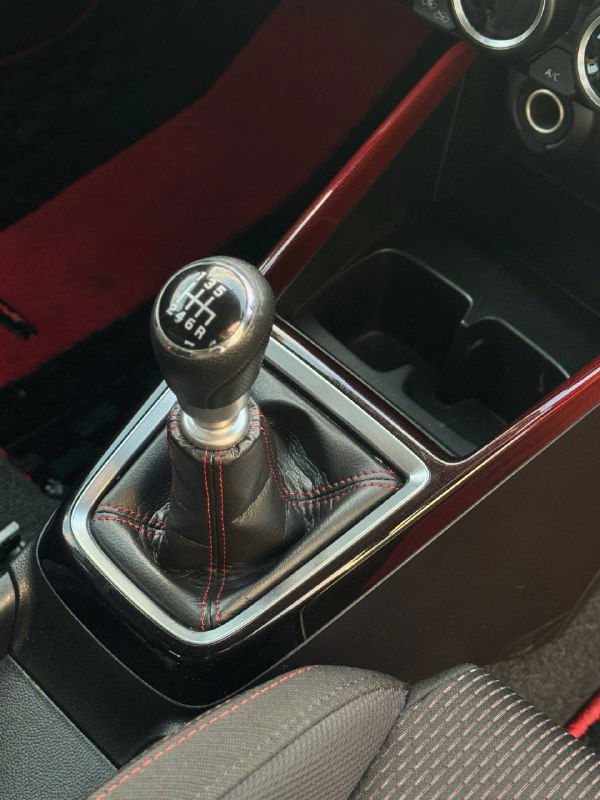 Рычаг механической коробки передач Suzuki Swift с кожаным чехлом и красной декоративной строчкой, центральный тоннель и подстаканники в кадре.