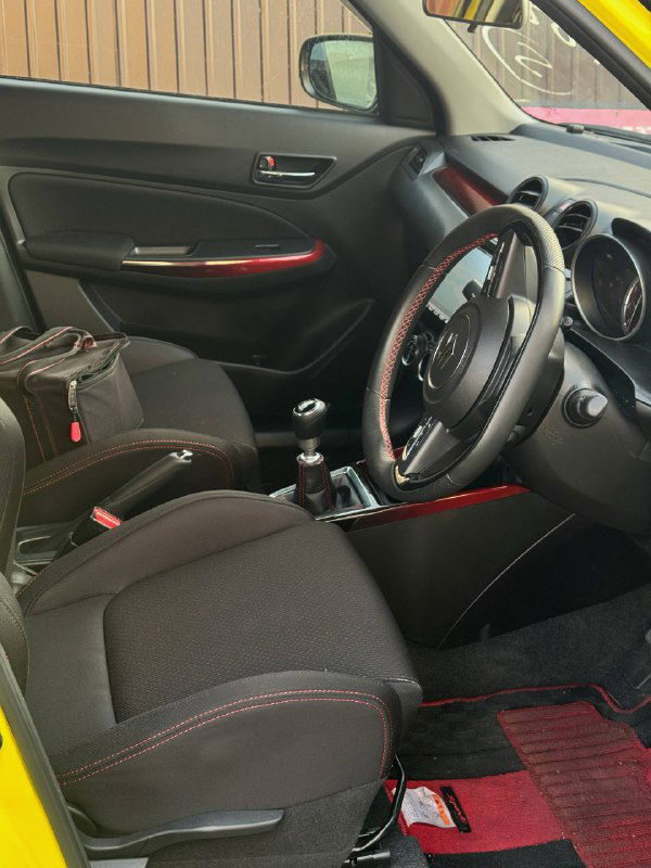 Переднее пассажирское кресло и центральная консоль Suzuki Swift, вид на обивку сидений, ручной тормоз и декоративные вставки красного цвета.